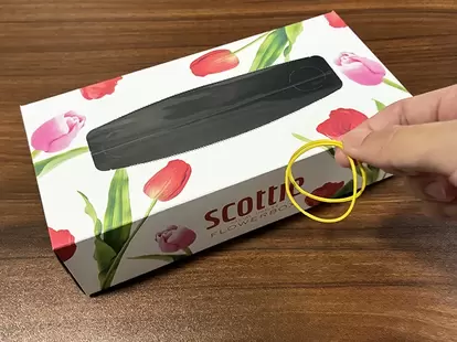 机に置いたティッシュの空き箱と、指で持った輪ゴム(撮影:grapeライフハック編集部)